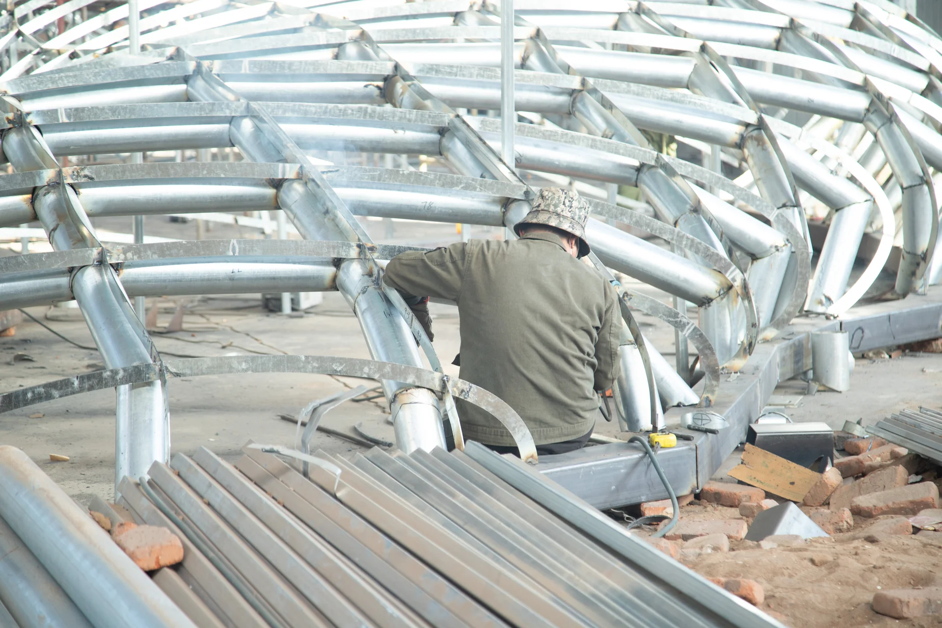 Worker welding the internal frame of a large stainless steel sculpture